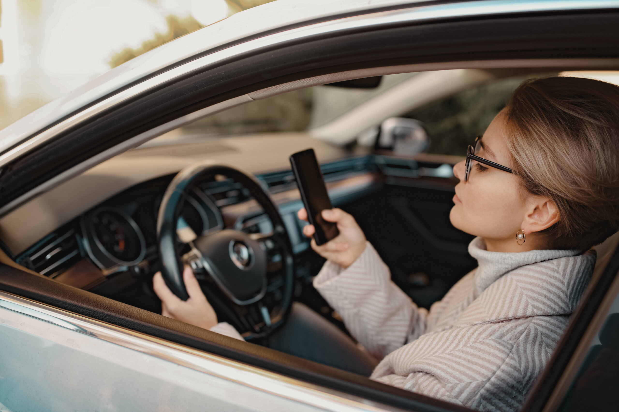 attractive stylish woman sitting in car dressed in coat Mujer conduciendo mientras revisa su celular