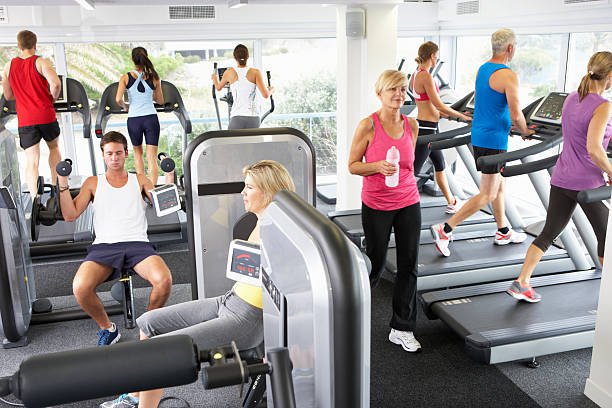 Un gimnasio abarrotado con muchas personas haciendo ejercicio y usando máquinas simultáneamente. 