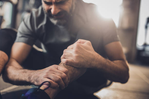 Un hombre en un gimnasio sufriendo una lesión en la pierna, agarrándose el tobillo con dolor.