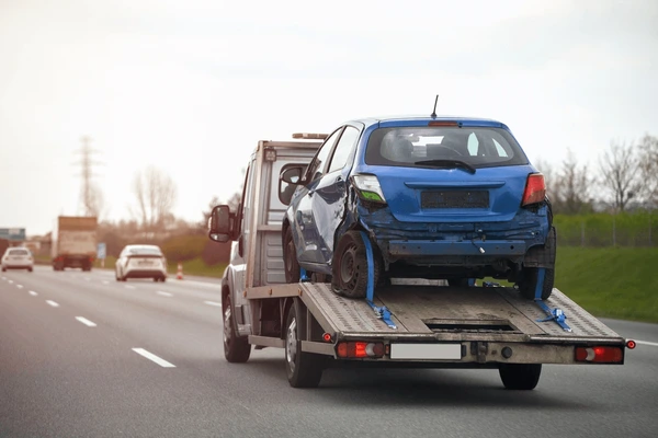 Grúa conduciendo en la carretera mientras lleva un auto azul dañado Estas son algunas de las causas más comunes detrás de los accidentes de grúas