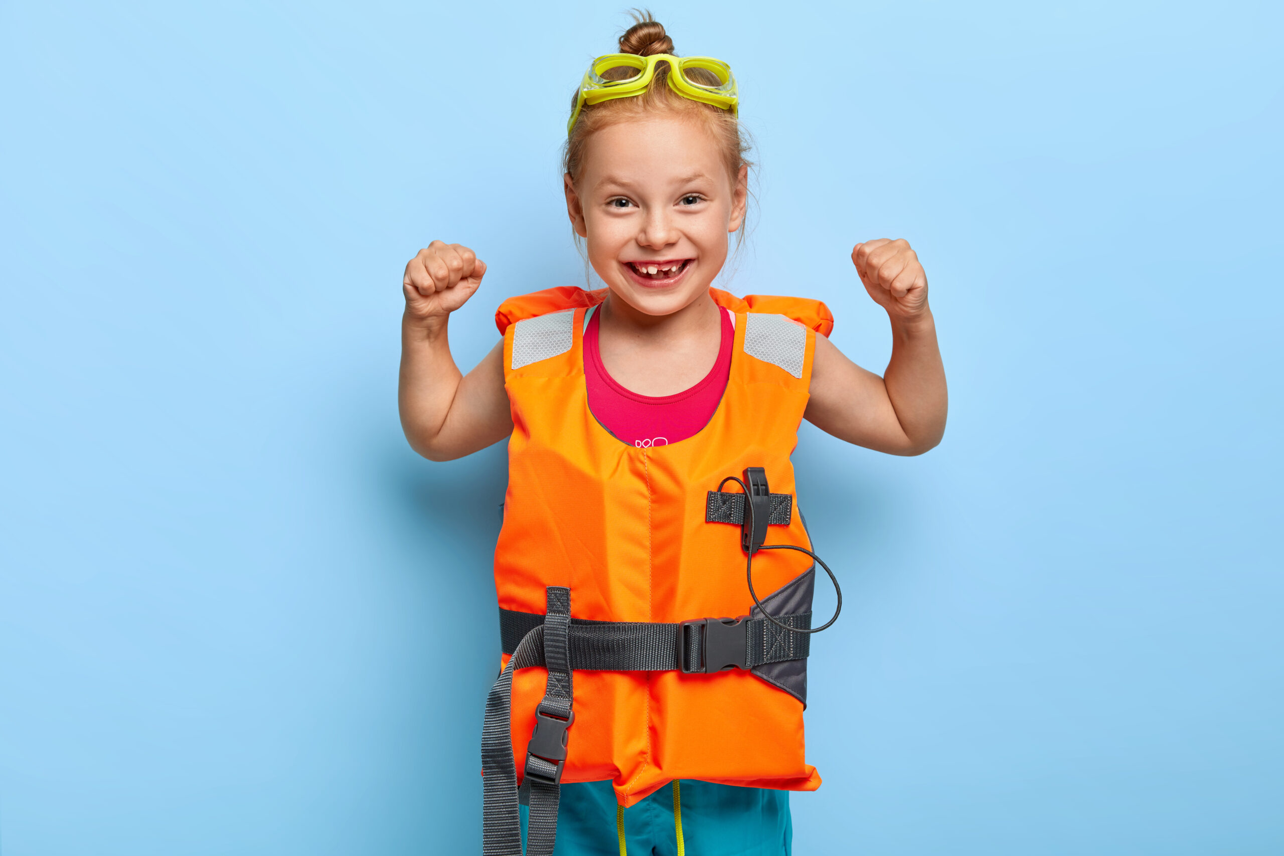 Niña sonriente usando un chaleco salvavidas de color naranja brillante y con lentes de natación amarillos en la cabeza