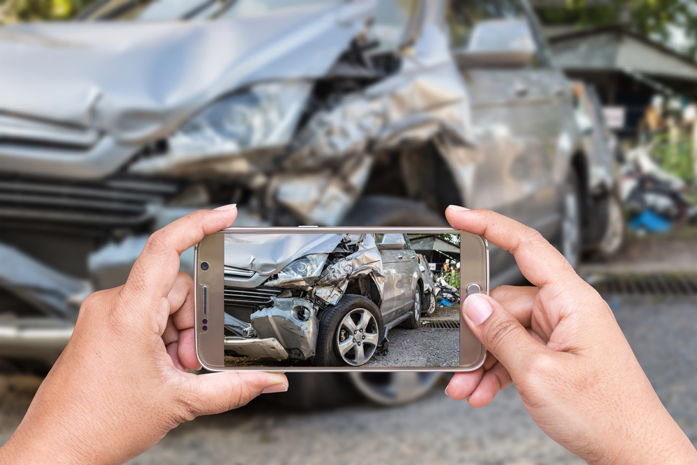 Manos usando un teléfono inteligente para fotografiar el grave daño frontal de un accidente de auto para un reclamo de seguro