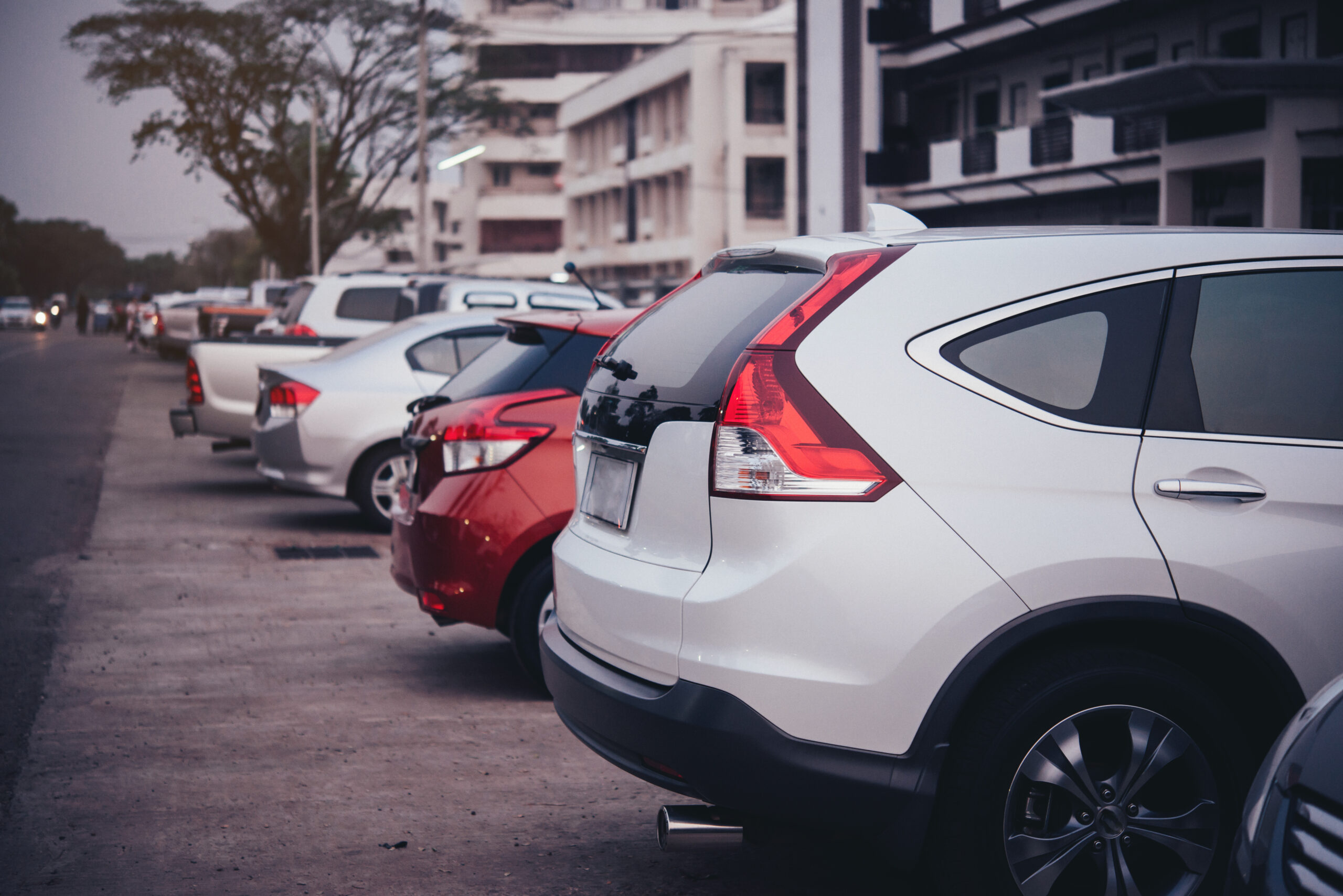Estacionamiento urbano con una SUV blanca y otros vehículos alineados frente a edificios