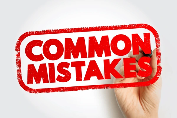 Mano escribiendo las palabras "Errores Comunes" (Common Mistakes) en un borde de estilo sello de goma rojo sobre un fondo blanco