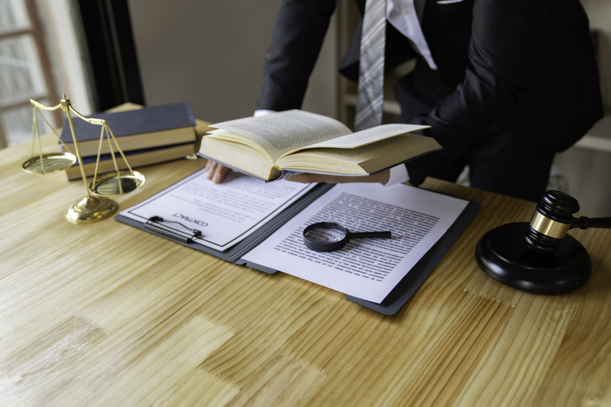 Abogado revisando documentos legales y un libro de leyes en un escritorio con mazo y balanza, representando análisis de casos, investigación legal y servicios de abogado