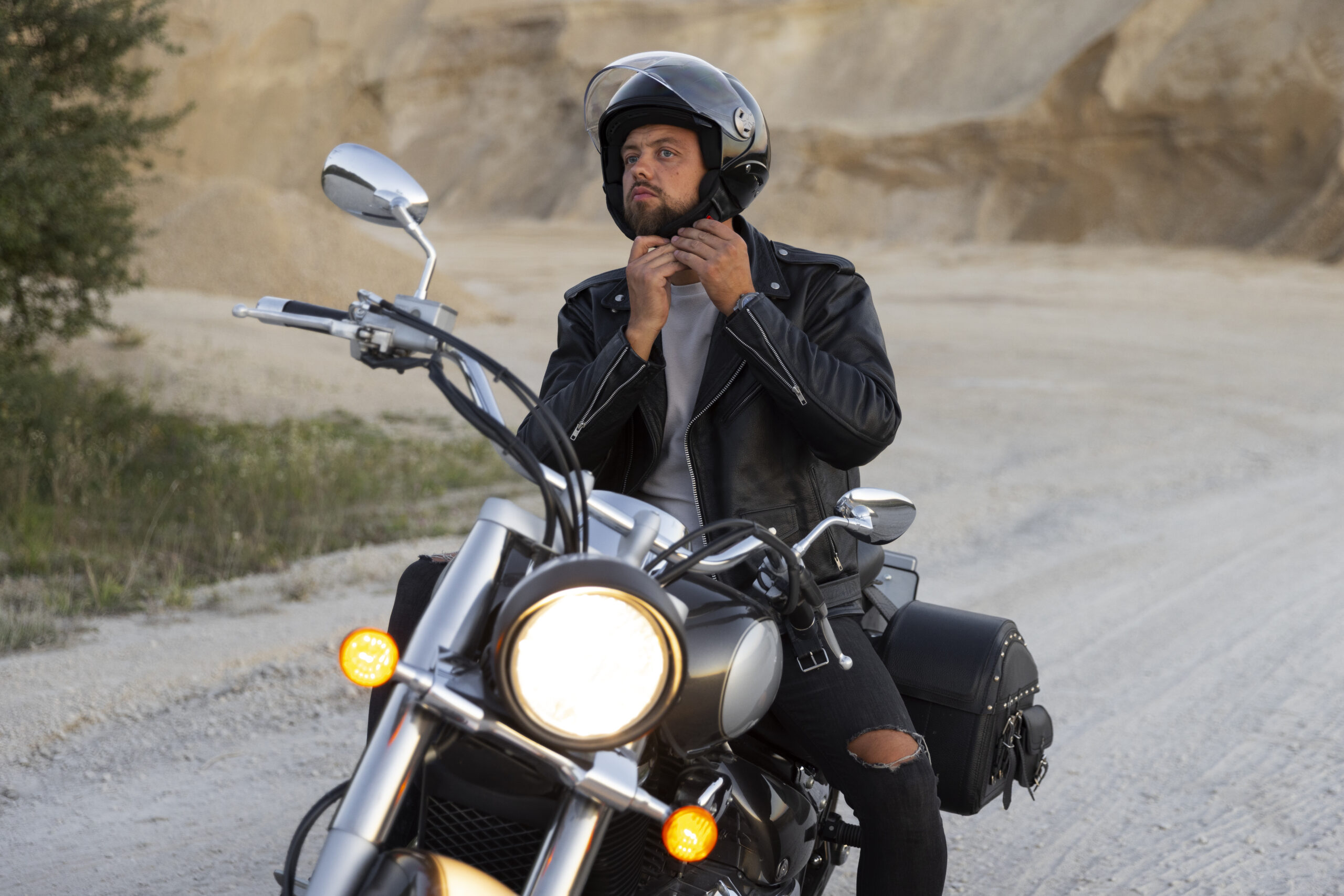 Hombre usando casco y chaqueta de cuero ajustando la correa mientras está sobre una motocicleta, resaltando la importancia del equipo de seguridad