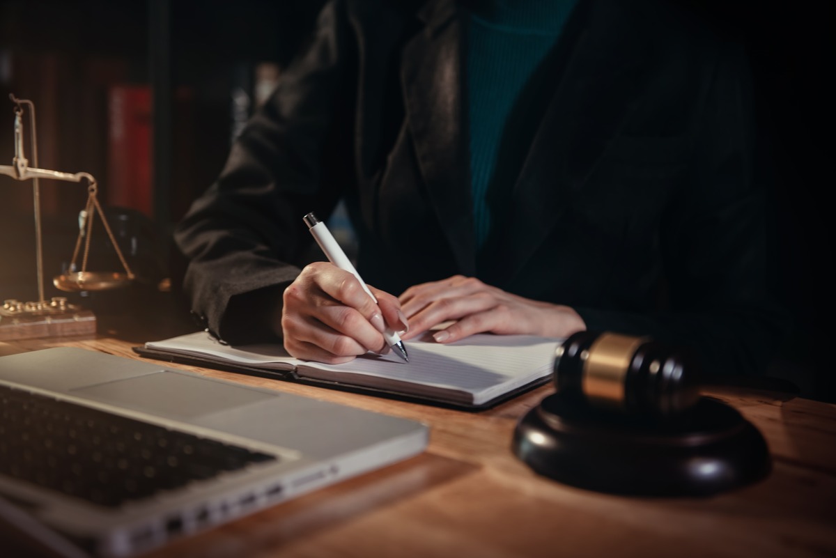 Abogado tomando notas en un escritorio con mazo, balanza de justicia y laptop, representando consulta legal, preparación de casos y servicios legales