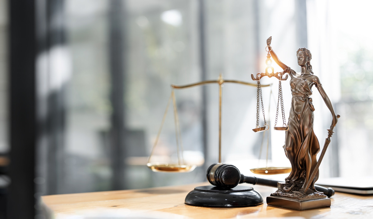 Estatua de la justicia con balanza y espada junto a un mazo de juez sobre un escritorio, representando el sistema legal, equilibrio y autoridad judicial