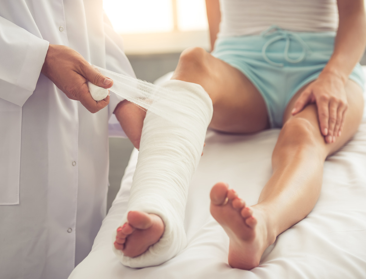 Médico colocando un yeso en la pierna de un paciente lesionado durante un tratamiento médico, ilustrando atención ortopédica, recuperación de lesiones, rehabilitación y reclamos por accidentes de lesiones personales