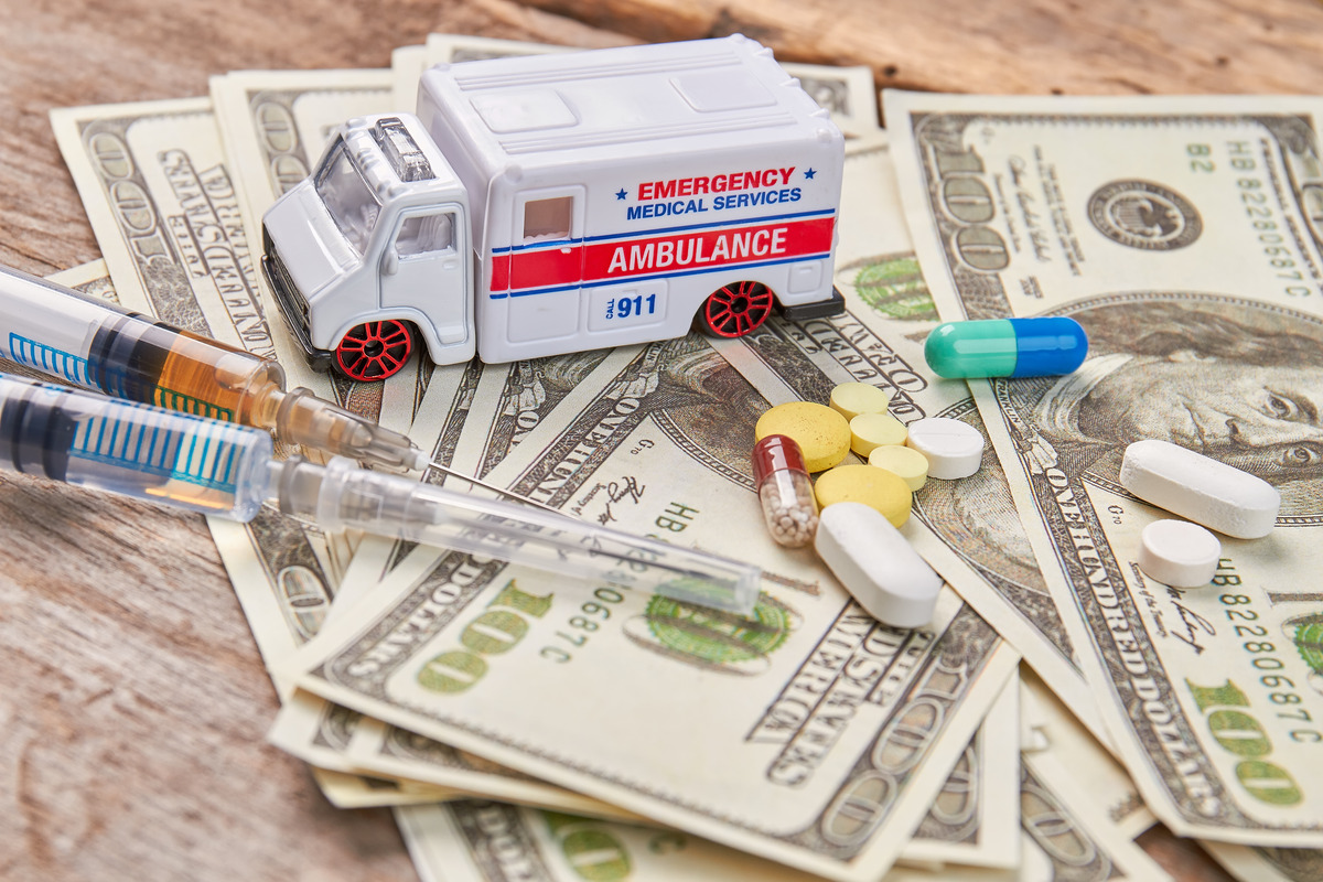 Concepto de gastos médicos y costos de atención médica con ambulancia, jeringas, medicamentos recetados y billetes estadounidenses, representando atención médica de emergencia, gastos de tratamiento, reclamos de seguros y financiamiento de la atención médica