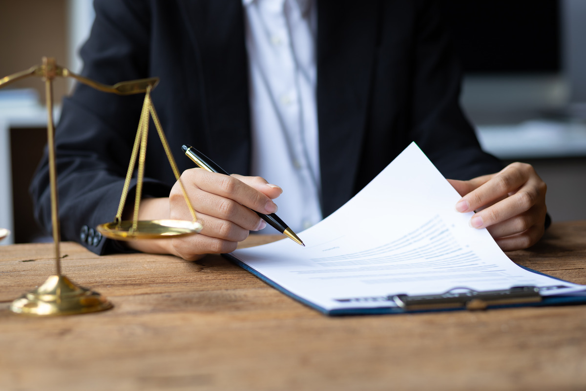 Abogado revisando documentos legales en un escritorio junto a una balanza de la justicia, representando consulta legal, evaluación de casos, revisión de contratos, servicios legales y representación profesional