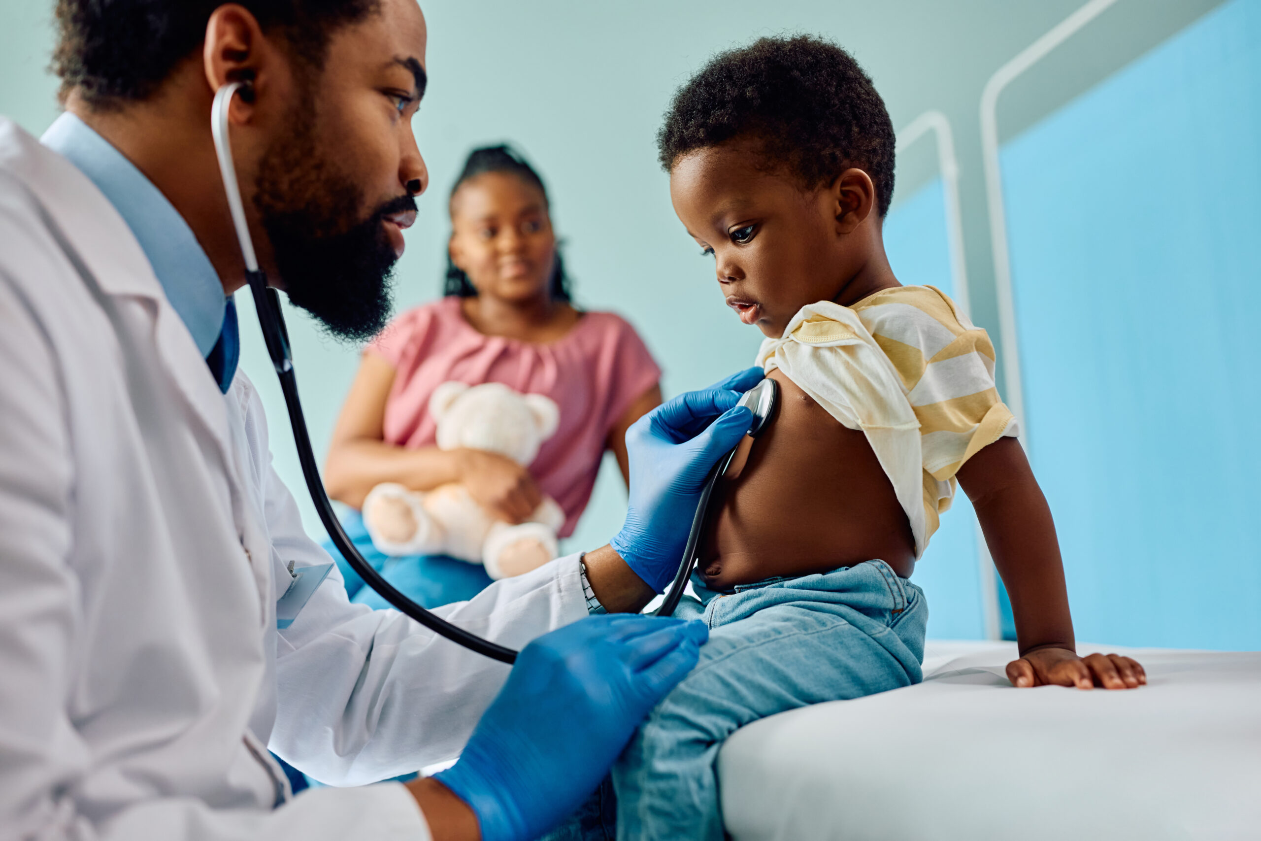 Niño recibiendo un examen médico de un pediatra con estetoscopio mientras uno de sus padres observa, representando atención médica pediátrica, chequeos de bienestar infantil, medicina familiar y atención preventiva