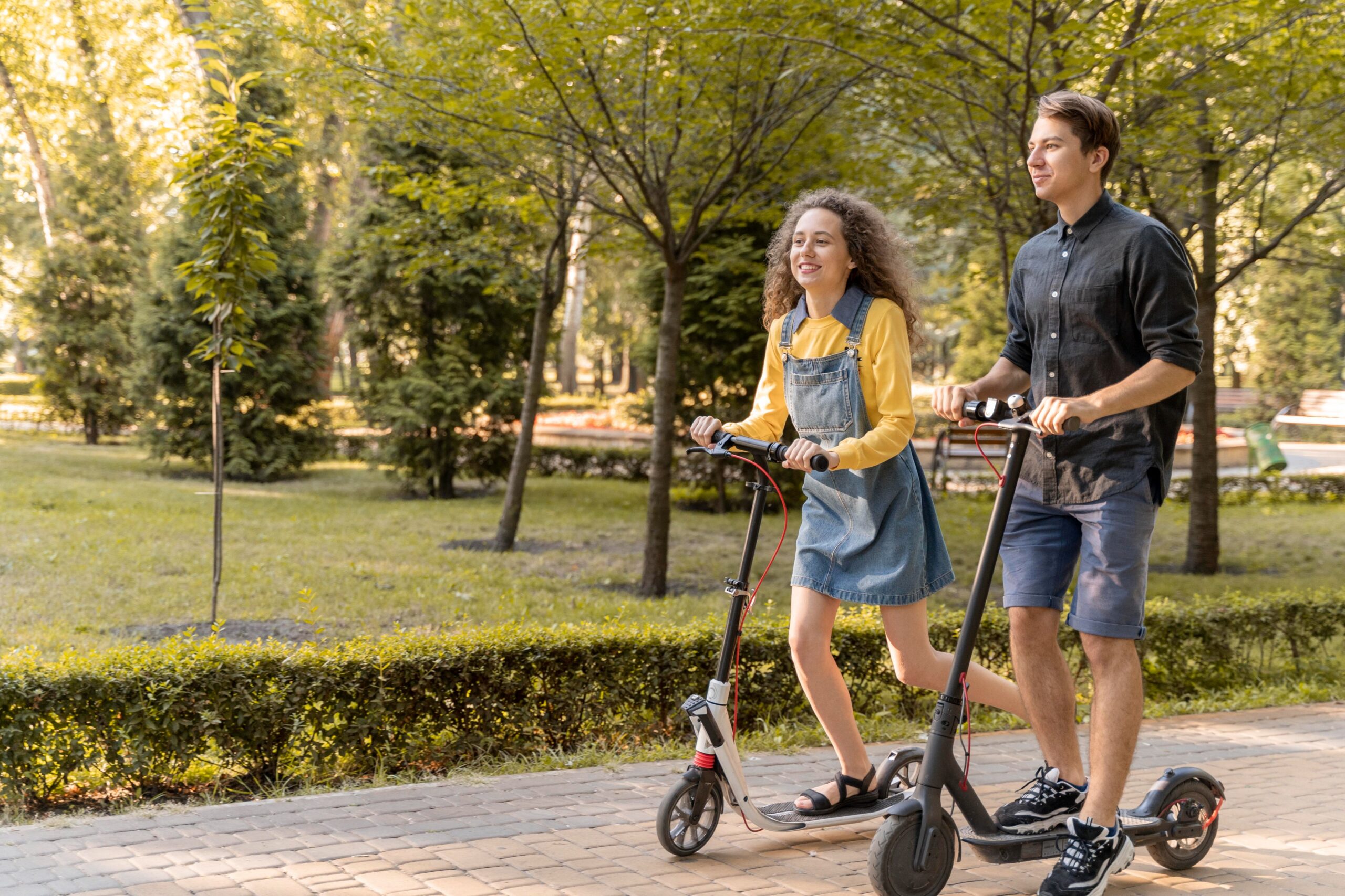 Dos personas conduciendo scooters eléctricos en un sendero de parque, representando transporte ecológico, uso recreativo de scooters eléctricos, movilidad urbana y consideraciones de seguridad para los usuarios de e-scooters.