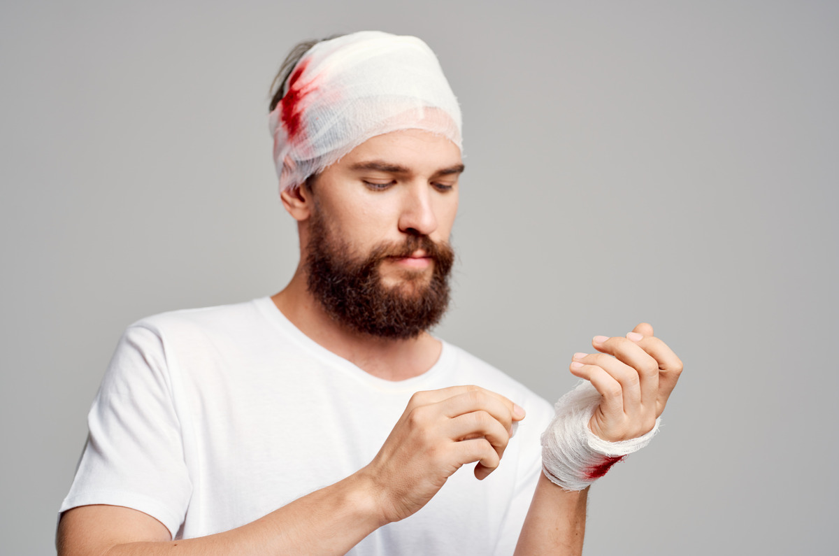 Hombre con un vendaje en la cabeza y la muñeca inmovilizada después de un accidente, representando una lesión cerebral traumática, traumatismo craneal, recuperación tras una lesión personal, tratamiento médico de emergencia y reclamaciones por lesiones relacionadas con accidentes.